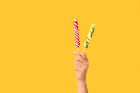 Hand with sweet lollipops on color background