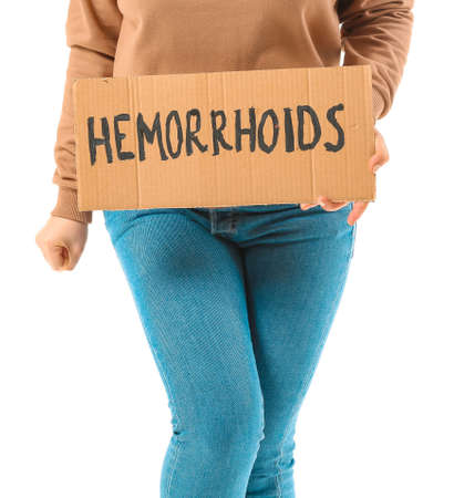 Young woman holding paper with text HEMORRHOIDS on white backgroundの写真素材