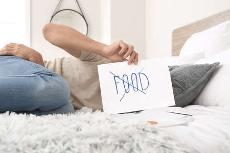 Sick man holding paper sheet with crossed word FOOD in bedroom. Concept of anorexiaの写真素材
