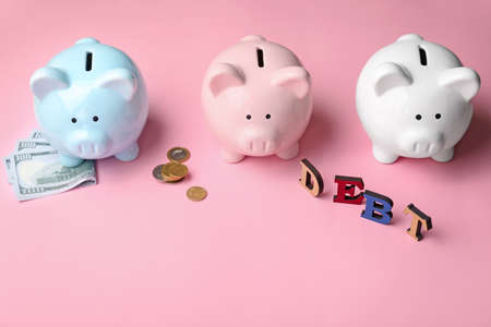 Piggy banks with money and word DEBT on color backgroundの写真素材