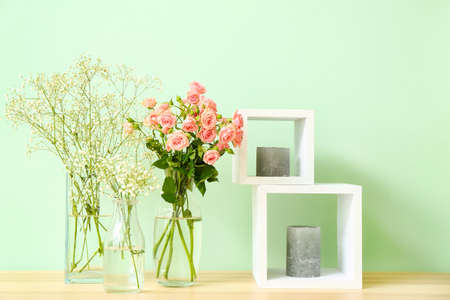 Stylish vases with beautiful flowers and candles on table near color wallの写真素材