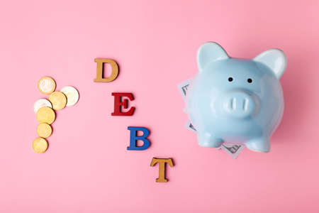 Piggy bank with money and word DEBT on color backgroundの写真素材