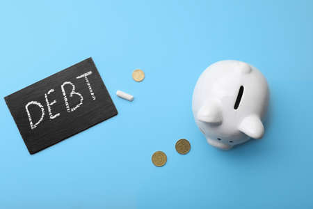 Piggy bank with coins and chalkboard with written word DEBT on color backgroundの写真素材