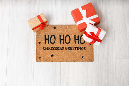 Door mat with Christmas greeting and gift boxes on wooden floorの写真素材