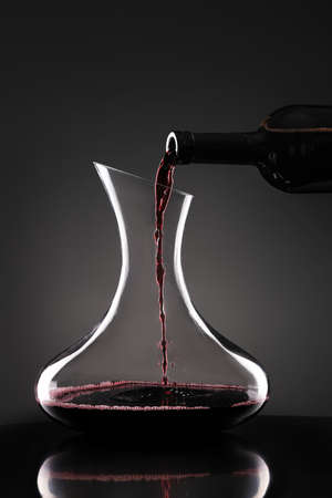 Pouring of tasty wine from bottle into glass on dark backgroundの写真素材
