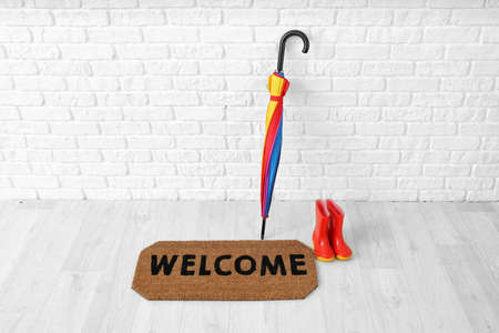 Door mat, gumboots and umbrella near white brick wallの写真素材