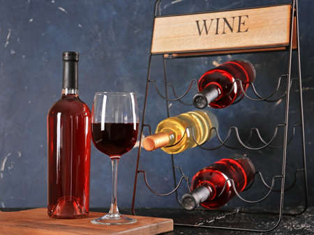 Holder with bottles and glass of wine on dark background