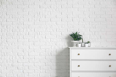 Green houseplants on chest of drawers near white brick wallの写真素材