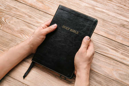 Hands of man with Bible on wooden background