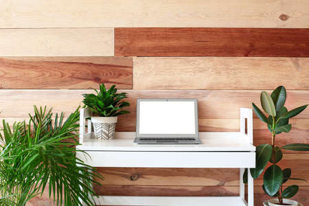 Comfortable workplace with modern laptop and houseplants near wooden wallの写真素材