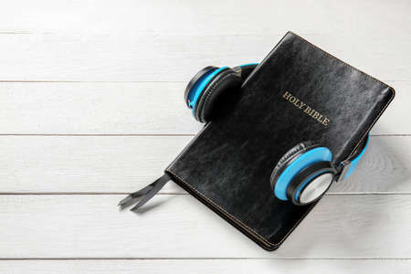 Holy Bible and headphones on white wooden background