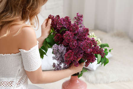 Beautiful young woman with bouquet of lilac flowers at homeの写真素材