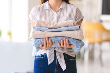 Woman with stack of clean clothes at home, closeup