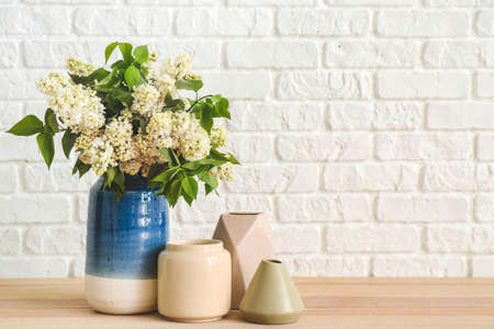 Vases with beautiful flowers on table near white brick wallの写真素材