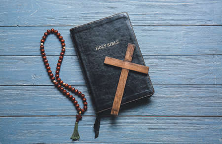 Holy Bible, cross and rosary beads on wooden background