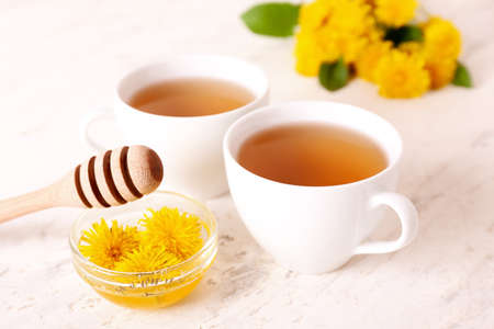 Cups of healthy dandelion tea with honey on light background