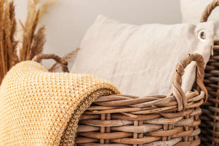 Wicker basket with pillow and plaid in room, closeup