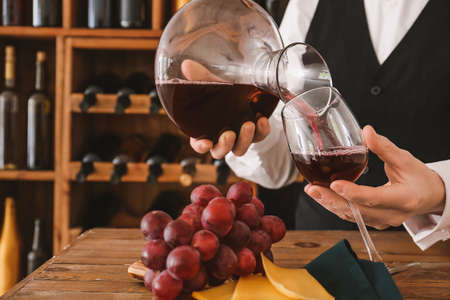 Sommelier pouring wine from decanter into glass in cellarの写真素材