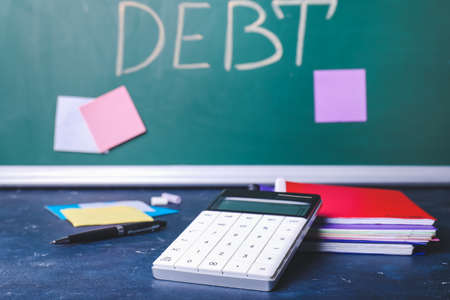 Notebooks, calculator and chalkboard with word DEBT on table