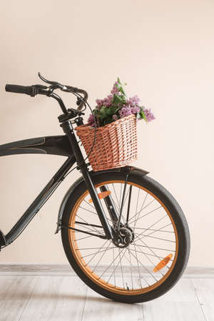 Modern bicycle and wicker basket with flowers near light wallの写真素材