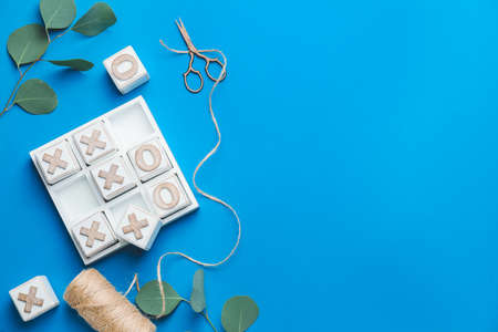 Scissors with threads and noughts-and-crosses game on color background