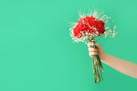 Female hand with bouquet of beautiful flowers on color backgroundの写真素材