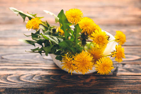 Bowl with beautiful dandelions on wooden backgroundの写真素材