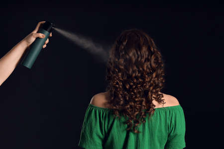 Beautiful young woman and hand with hair spray on dark backgroundの写真素材