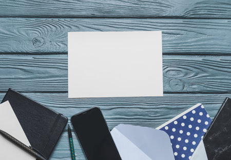 Blank card with envelope, mobile phone and stationery on wooden backgroundの写真素材