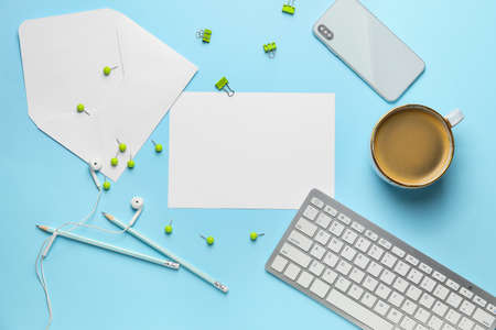 Blank card with envelope, stationery, cup of coffee and computer on color backgroundの写真素材