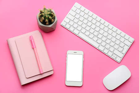 Modern mobile phone with computer and notebook on color background