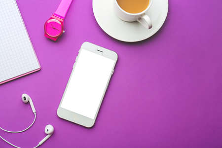 Modern mobile phone with earphones, clock and cup of coffee on color backgroundの写真素材