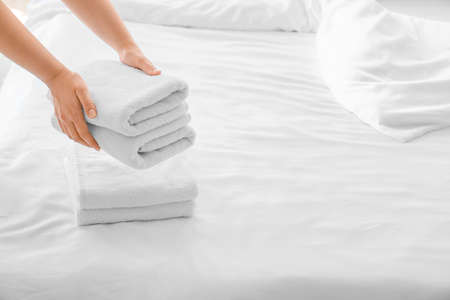 Woman putting clean towels on bed at home