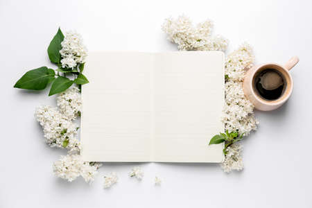 Notebook, beautiful lilac flowers and cup of coffee on white backgroundの写真素材