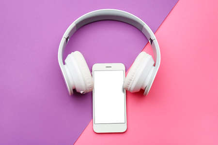 Modern mobile phone with headphones on color background