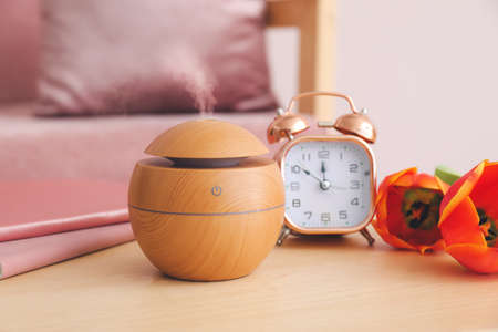 Aroma oil diffuser, clock and flowers on table in room