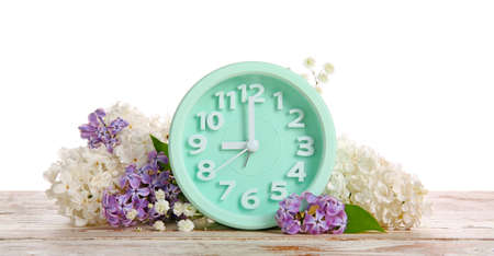 Alarm clock and flowers on table against white background. Spring time