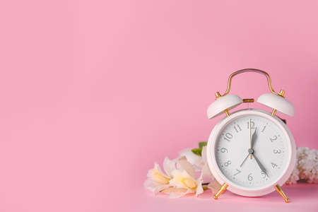 Alarm clock and flowers on color background. Spring timeの写真素材