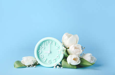 Alarm clock and flowers on color background. Spring timeの写真素材