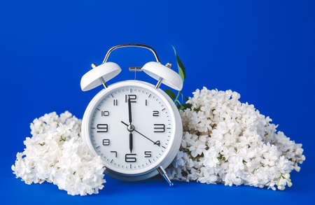 Alarm clock and flowers on color background. Spring time