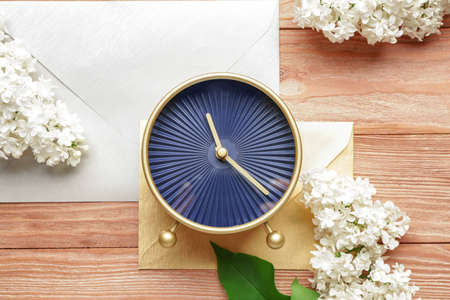 Alarm clock and flowers with envelopes on wooden background. Spring time