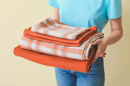Woman holding stack of clean bed sheets on color background
