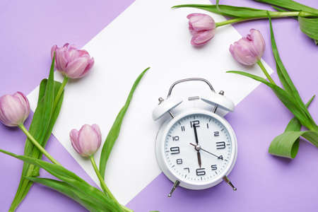Alarm clock and flowers on color background. Spring time