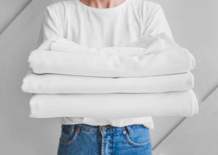 Woman with stack of clean bed sheets on light backgroundの写真素材