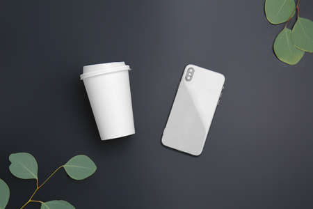 Takeaway cup for drink and mobile phone on dark background