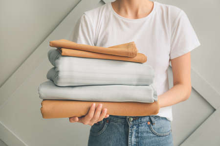 Woman with stack of clean bed sheets on light backgroundの写真素材