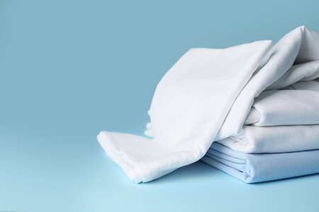 Stack of clean bed sheets on color background