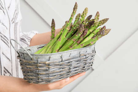 Woman with basket of fresh asparagus on light backgroundの写真素材