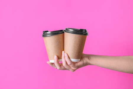 Hand with takeaway cups for drink on color backgroundの写真素材