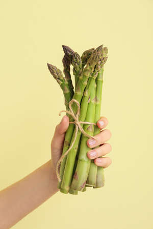 Hand with fresh asparagus on color backgroundの写真素材